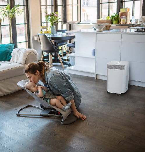 A mother kisses her baby in a living room while an INOVA Air Purifier quietly cleans the air, removing dust and bacteria.