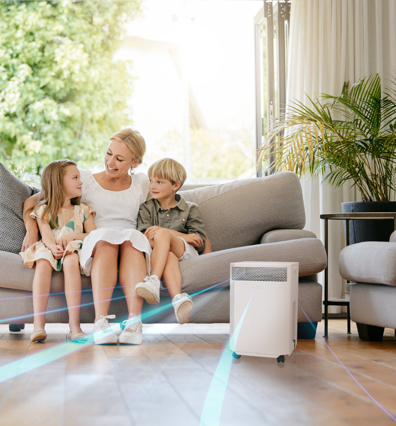Load image into Gallery viewer, A mother sitting on a couch with her two young children with an INOVA air purifier in the foreground quietly cleaning the air around them.