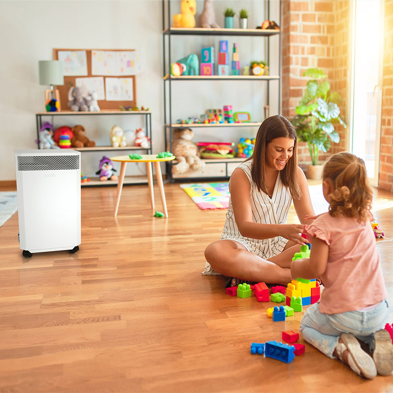 Load image into Gallery viewer, A children's playroom where a young woman plays with brightly coloured blocks, entertaining a small child. In the background, an INOVA air purifier quietly cleans the air, removing harmful dust particles, viruses and bacteria.