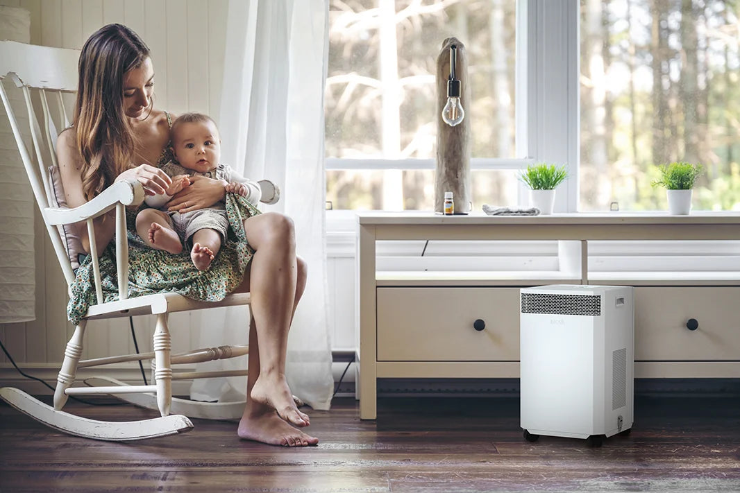 mother holds baby in chair near inova e8 air purifier