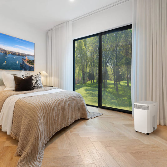 A comfortable warm bedroom with a window looking out to a grassy area. An INOVA air purifier sits on the floor, quietly cleaning the air, removing dust, allergens and bacteria.